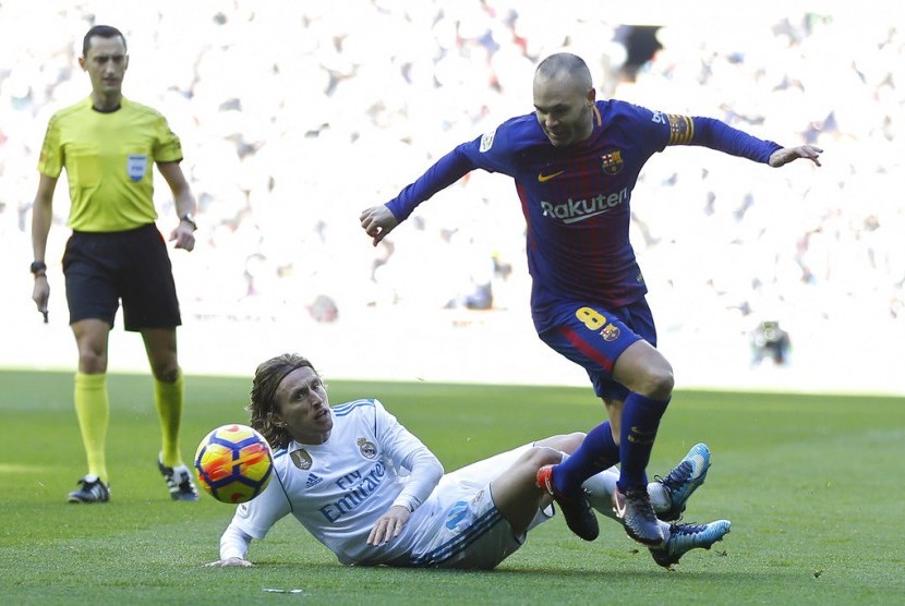 Kapten Barcelona, Andres Iniesta (kanan) berusaha dijegal oleh gelandang Real Madrid, Luka Modric pada laga el Clasico di Santiago Bernabeu, Sabtu (23/12). Barca menang 3-0 pada laga ini.