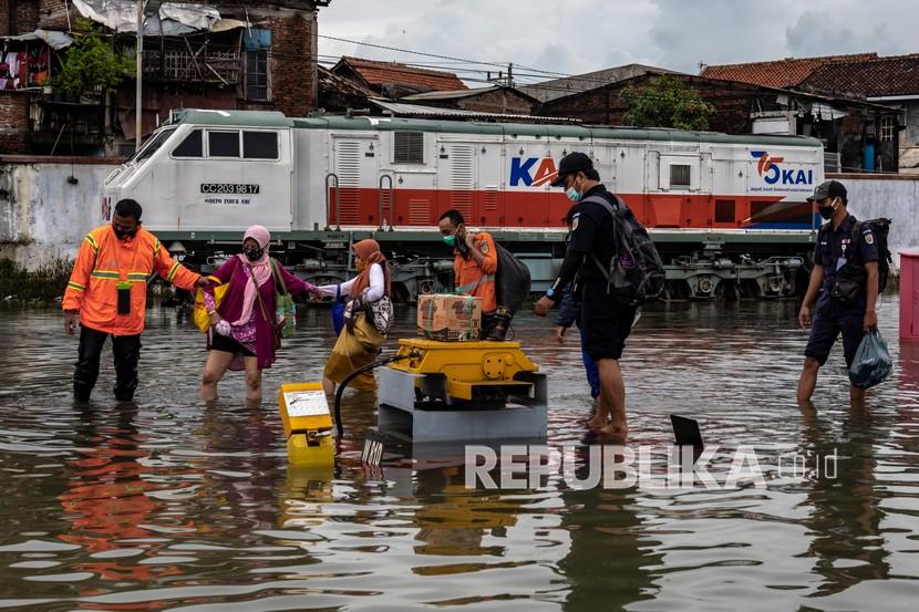 Karyawan membantu sejumlah penumpang menembus banjir untuk keluar dari Stasiun Tawang yang terendam banjir di Semarang, Jawa Tengah, Sabtu (6/2/2021). Akibat banjir setinggi hingga 70 cm tersebut, PT KAI (Persero) DAOP 4 Semarang mengalihkan sejumlah rute perjalanan kereta api.