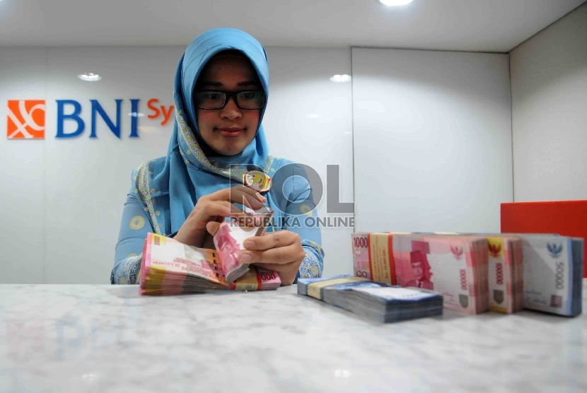 Karyawan menghitung uang di Banking Hall Bank BNI Syariah, Jakarta.