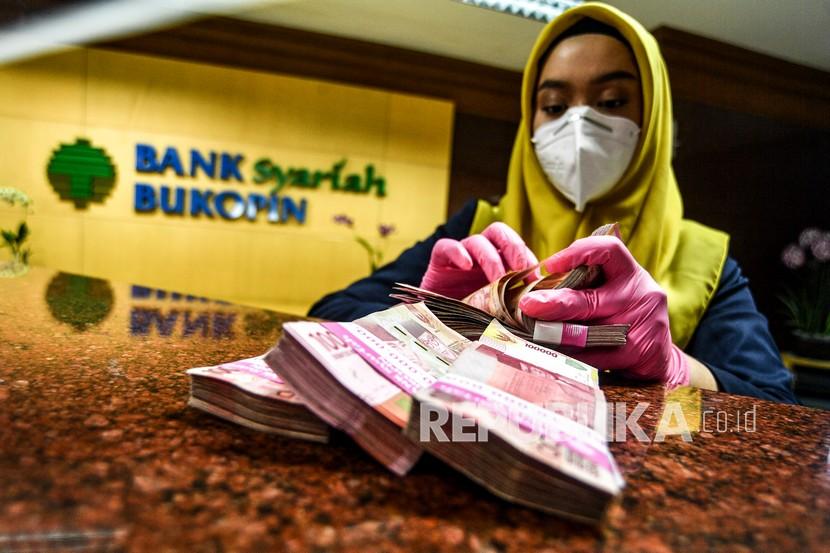 Karyawan menghitung uang pecahan Rp100 ribu dari setoran nasabah di Bank Bukopin Syariah, Jakarta (ilustrasi).