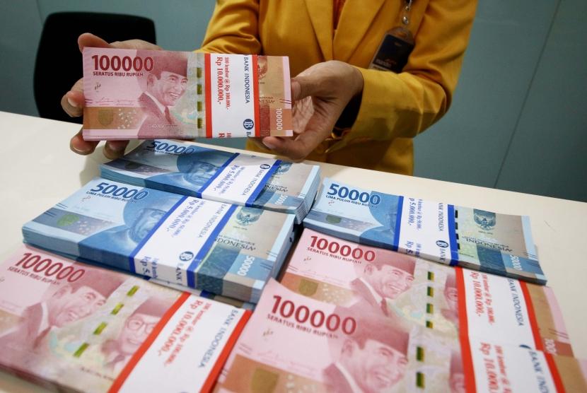 Karyawan menunjukan uang rupiah pecahan 100 ribu dan 50 ribu.