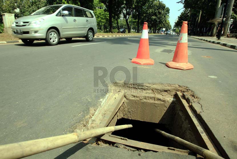 Kendaraan melintas di lubang saluran air di Jalan Sudirman, Jakarta, Selasa (1/7).