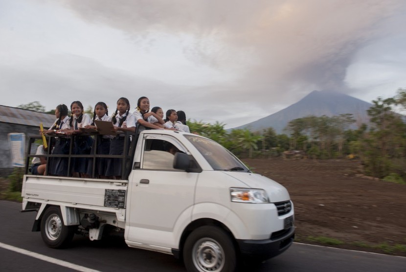 Kendaraan mengangkut siswa dengan latar belakang asap dan abu vulkanik menyembur dari kawah Gunung Agung di Desa Datah, Karangasem, Bali, Senin (27/11). 