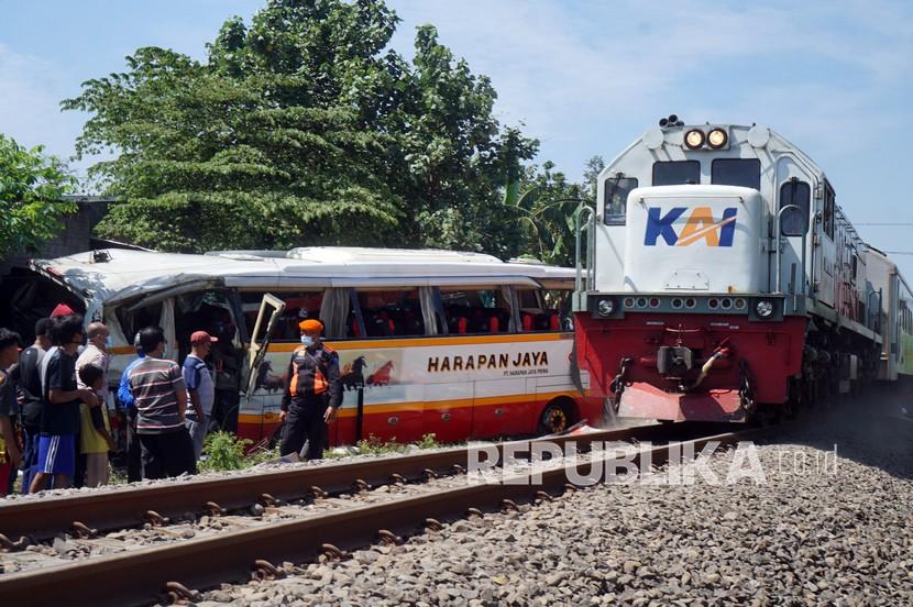 Kereta api melintas dekat bangkai bus pariwisata PO Harapan Jaya yang tertabrak KA Rapih Doho di perlintasan kereta api tanpa palang pintu di Desa Ketanon, Tulungagung, Jawa Timur, Ahad (27/2/2022). Kecelakaan yang terjadi sekitar pukul 05.00 WIB itu menyebabkan lima dari 43 penumpang termasuk awak bus meninggal dunia dan 14 lainnya luka-luka dan harus dilarikan ke RSUD dr. Iskak Tulungagung untuk mendapat pertolongan kedaruratan medis.