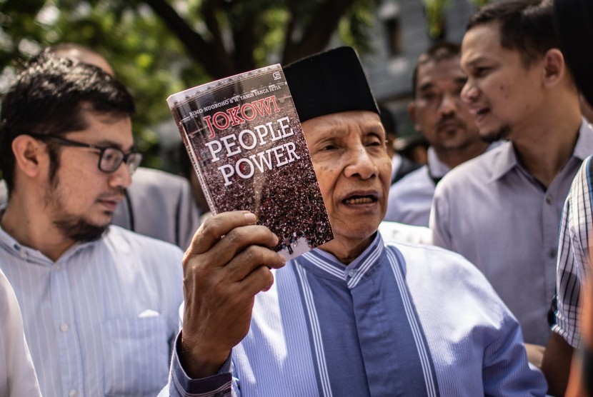 Ketua Dewan Kehormatan Partai Amanat Nasional (PAN) Amien Rais (tengah) menunjukkan buku berjudul Jokowi People Power saat jeda pemeriksaan untuk Shalat Jumat di Direktorat Reserse Kriminal Umum (Ditreskrimum) Polda Metro Jaya, Jakarta, Jumat (24/5/2019). 