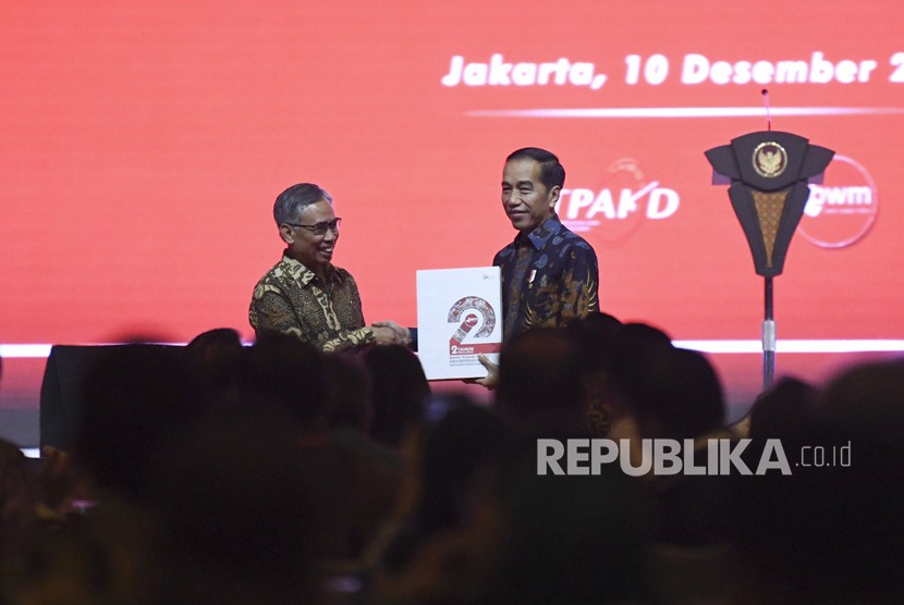 Ketua Dewan Komisioner Otoritas Jasa Keuangan (OJK) Wimboh Santoso (kiri) menyerahkan buku dua tahun Bank Wakaf Mikro (BWM) kepada Presiden Joko Widodo (kanan) saat Rapat Koordinasi Nasional Tim Percepatan Akses Keuangan Daerah (TPAKD) dan Silahturahmi Nasional Bank Wakaf Mikro 2019 di Jakarta, Selasa (10/12/2019).