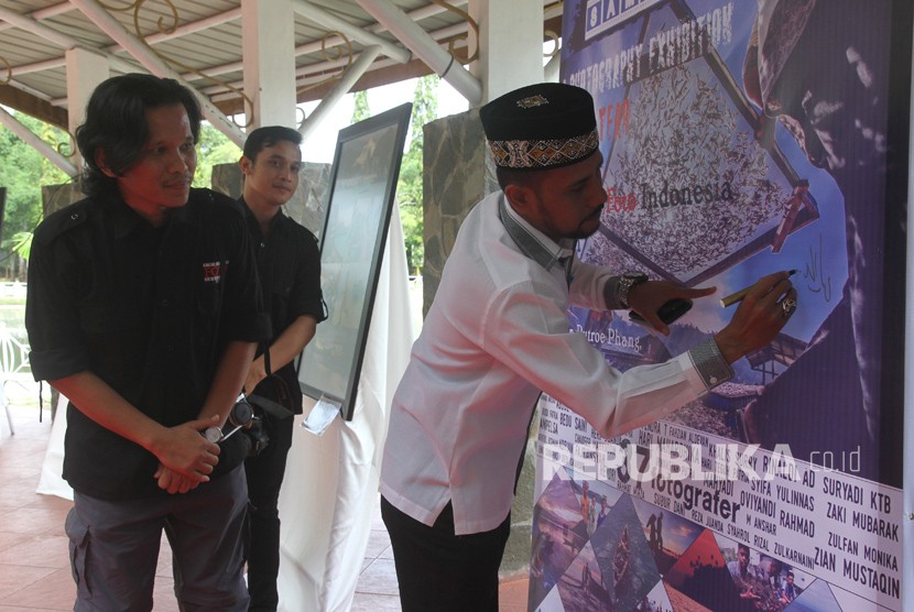 Ketua Dewan Perwakilan Rakyat Aceh (DPRA) Muharuddin (kanan) didampingi Ketua Pewarta Foto Indonesia (PFI) Aceh Fendra Trysani (kiri) menandatangi banner pemeran foto peringati tsunami sebagai pertanda pembukaan pameran di Taman Putroe Phang, Banda Aceh, Aceh, Senin (25/12).