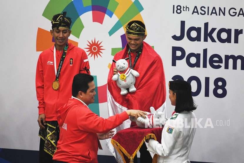 Ketua INASGOC Erick Tohir (kiri bawah) memberikan medali emas kepada pasangan pesilat Indonesia peraih medali emas Yola Primadona Jampil (kanan atas)-Hendy (kiri atas) saat upacara penyerahan medali nomor tunggal putri pencak silat seni Asian Games 2018 di Padepokan Pencak Silat Taman Mini Indonesia Indah (TMII), Jakarta, Senin (27/8).