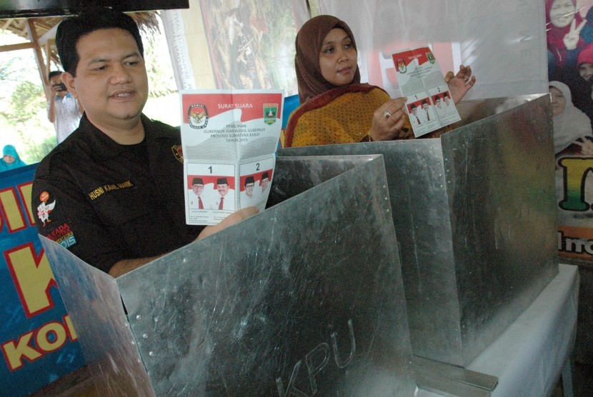 Ketua KPU Pusat Husni Kamil Manik (kiri) dampingi istri Endah Mulyani, menunjukkan surat suara pemilihan gubernur Sumbar saat menggunakan hak pilih di TPS 06 Surau Gadang Siteba, Padang, Sumatera Barat, Rabu (9/12).