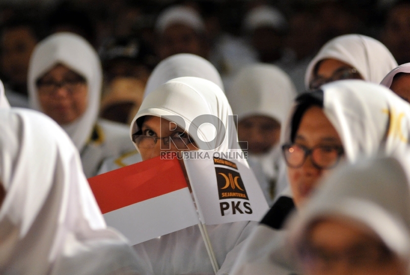  Seorang kader memegang bendera merah putih dan bendera Partai Keadilan Sejahtera (PKS). Pengamat menyarankan PKS melebarkan sayap ke pemilih nasionalis untuk naikkan suara.