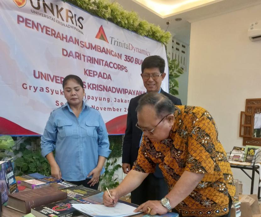 Ketua Pengurus Yayasan Unkris, Amir Karyatin SH, menandatangani serah terima bantuan buku disaksikan Direktur Trinitacorps Johanna Ambar dan Rektor Unkris Dr Ayub Muktiono (tengah).