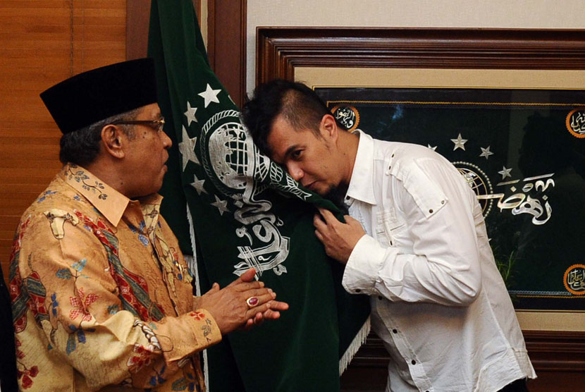  Ketua Umum PBNU, Said Aqil Siroj (kiri), menyaksikan Ketua Seni dan Kebudayaan NU, Ahmad Dhani (kanan), mencium bendera NU usai memberikan pin ketua Seni dan Kebudayaan dalam tasyakuran Harlah PBNU ke 91 di Jakarta, Jumat (16/5). 