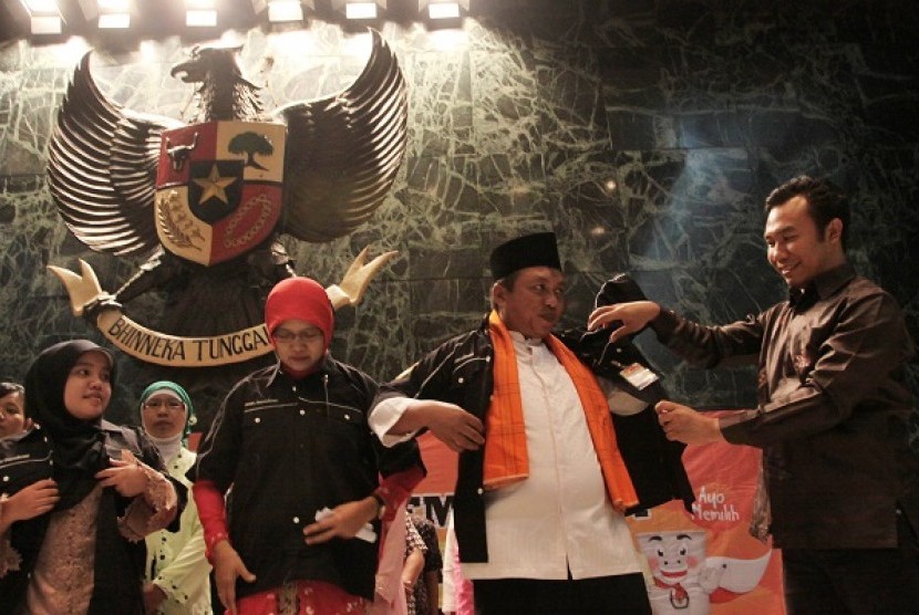 Komisioner KPU Sigit Pamungkas (kanan) mengenakan seragam kepada salah satu anggota masyarakat saat pengukuhan Relawan Demokrasi di Jakarta, Jumat (18/10).