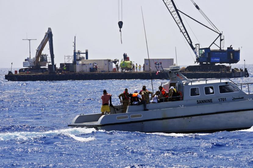 Korban selamat dengan anggota keluarga dari kapal migran yang tenggelam menonton dari kapal angkatan laut ketika pasukan angkatan laut Lebanon dan personel teknis bersiap untuk mengirim kapal selam ke Laut Mediterania untuk mencoba menemukan sekitar 30 mayat sekitar 450 meter di bawah permukaan di dalam kapal migran yang tenggelam pada malam hari empat bulan yang lalu sekitar lima km (3,1 mil) di luar pelabuhan Tripoli, dalam keadaan yang disengketakan, Lebanon utara, Senin, 22 Agustus 2022. Korban selamat menuduh tentara menenggelamkan kapal, tetapi tentara mengklaim kapal itu menabrak mereka.