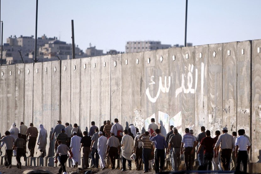 Laki-laki Palestina melintas disamping tembok pemisah Israel dalam perjalanan mereka untuk shalat Jumat di Masjid Al Aqsa di Yerusalem, Jumat (10/8). (Majdi Muhammad/AP)