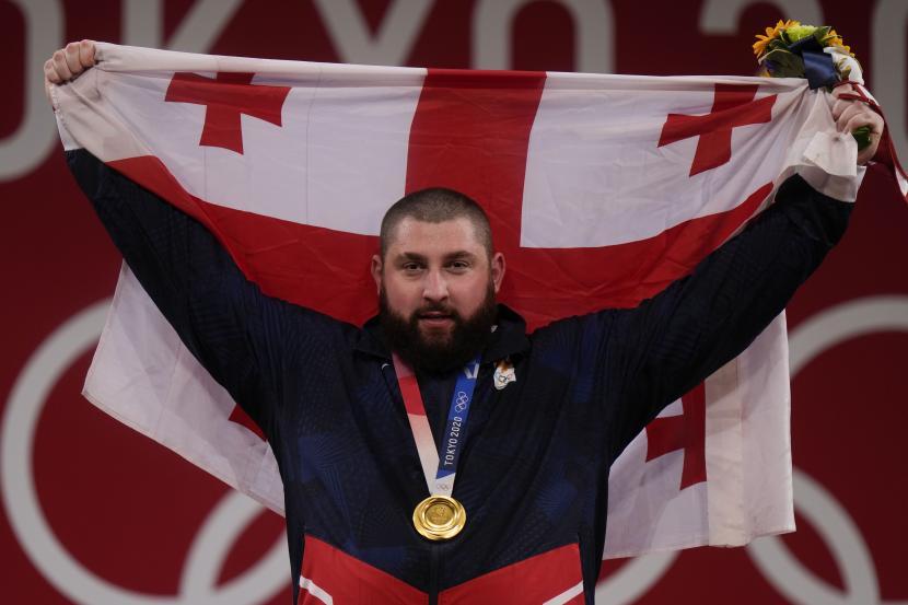 Lasha Talakhadze dari Georgia memegang bendera nasionalnya saat merayakan medali emas yang diraihnya di cabang angkat besi +109kg putra, di Olimpiade Musim Panas 2020, Rabu, 4 Agustus 2021, di Tokyo, Jepang.