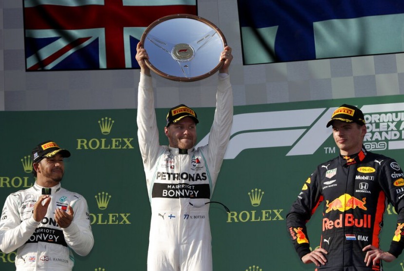 Lewis Hamilton (kiri) menyaksikan Valtteri Bottas mengangkat trofi juara GP Australia 2019.