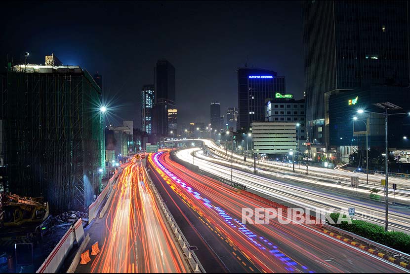 Lintasan sinar lampu mobil berpadu dengan lansekap kota malam hari.