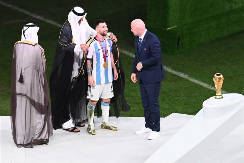 Lionel Messi dari Argentina menerima jubah tradisional Arab dari Tamim bin Hamad Al Thani (2-L), Emir Qatar, saat Presiden FIFA Gianni Infantino (kanan) melihat setelah Final Piala Dunia FIFA 2022 antara Argentina dan Prancis di stadion Lusail, Lusail, Qatar, Ahad (18/12/2022). Messi Pakai Jubah Arab Tuai Komentar Rasialis dari Media Inggris