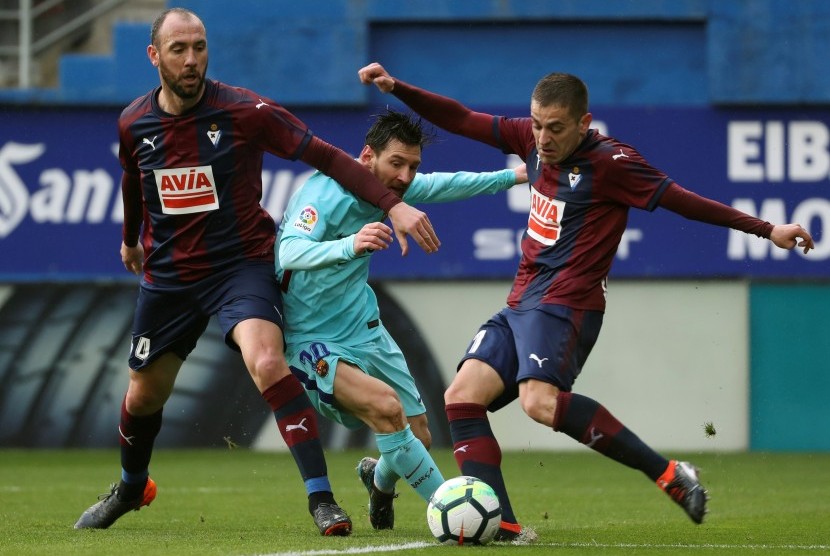 Lionel Messi (tengah) berebut bola dengan dua pemain Eibar, Ivan Ramis (kiri) dan Ruben Pena (kanan). 