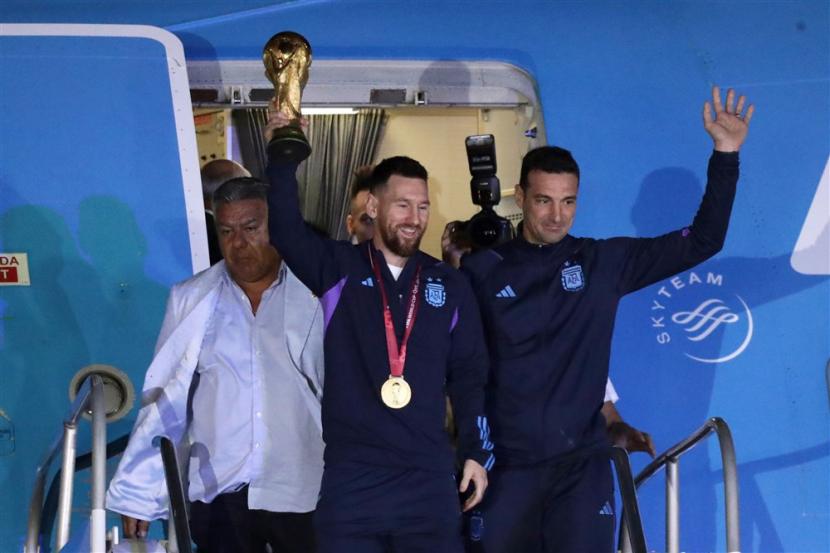 Lionel Messi (Tengah) dari tim sepak bola nasional Argentina turun pesawat dengan trofi Piala Dunia Qatar 2022 didampingi oleh pelatih kepala Lionel Scaloni (R), setibanya di Bandara Internasional Ezeiza, sekitar 22km dari Buenos Aires, Argentina, Selasa (20/12/2022).