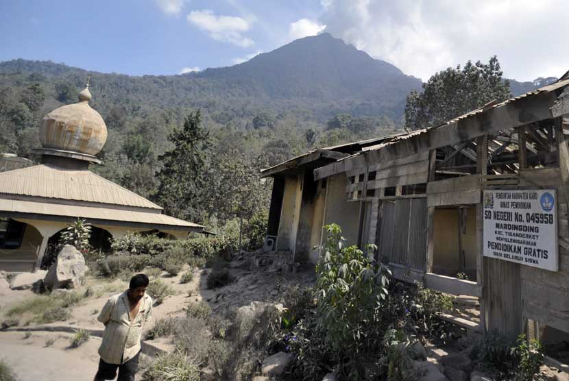 Seorang warga melintasi masjid dan sekolah dasar yang rusak akibat abu vulkanik Gunung Sinabung di Desa Mardinding, Karo, Sumut, Selasa (4/2).   (Antara/Wahyu Putro)