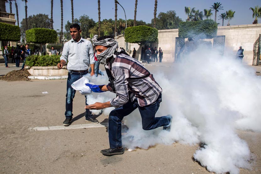   Pendukung Presiden terguling Muhammad Mursi mengambil tabung gas air mata yang ditembakkan oleh pasukan keamanan di Universitas Kairo, Giza, Mesir, Rabu (26/3).  (AP/Amru Taha)