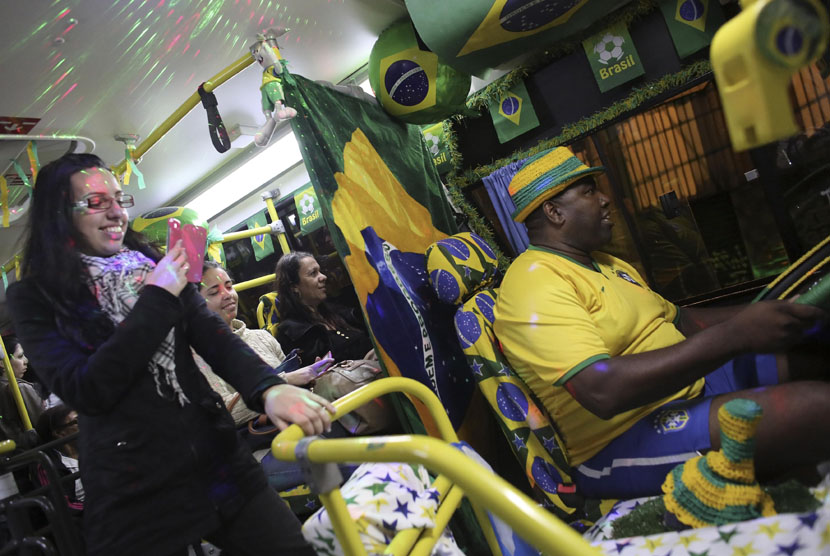   Sopir bus Edilson (kanan) mengenakan jersey timnas Brasil saat ia mengendarai sebuah bus kota yang dihiasi dengan warna bendera Brasil dan motif Piala Dunia 2014 di Santo Andre, pinggiran kota Sao Paulo, Rabu (18/6). (REUTERS/Nacho Doce)