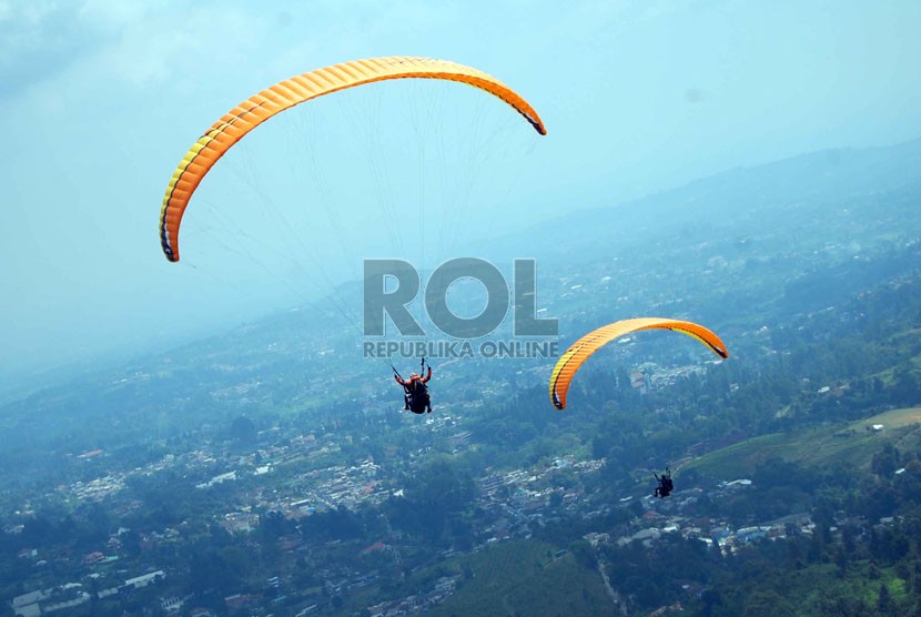 Pengunjung bersama pemandu wisata aero sport menerbangkan paralayang yang berada di kawasan Puncak Pass, Bogor, Sabtu (2/8). (Republika/Raisan Al Farisi)