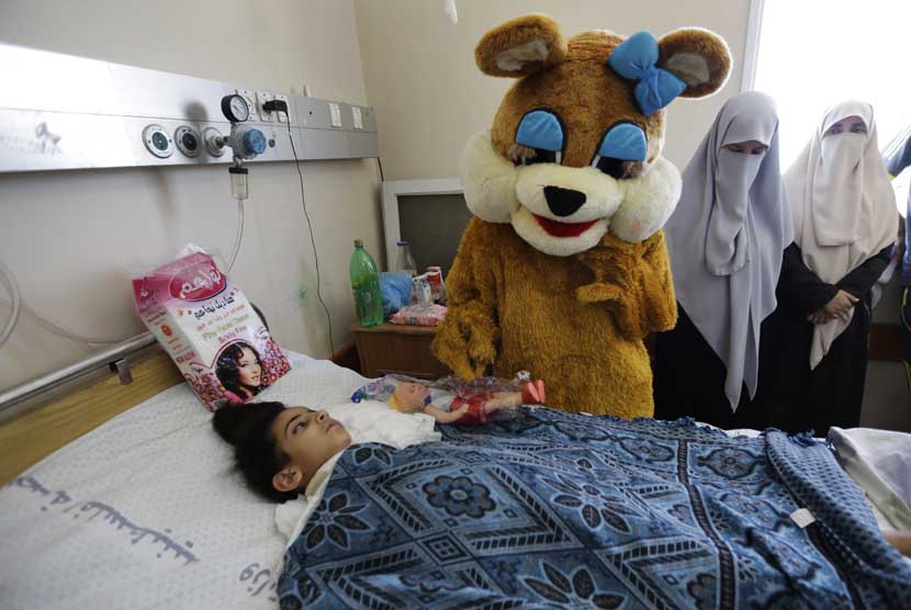 Maha al-Sheikh Khalil(7), kiri, menerima hadiah oleh seorang pekerja amal berpakaian sebagai beruang untuk liburan Idul Fitri di tempat tidur rumah sakit di Kota Gaza, di Jalur Gaza utara, Senin, 28 Juli, 2014.