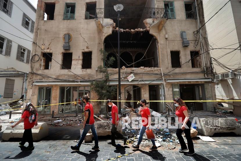 Mahasiswa yang secara sukarela membantu membersihkan rumah yang rusak dan memberi bantuan lainnya, lewat di depan gedung yang rusak akibat ledakan pekan lalu, di Beirut, Lebanon, Selasa (11/8/2020). 