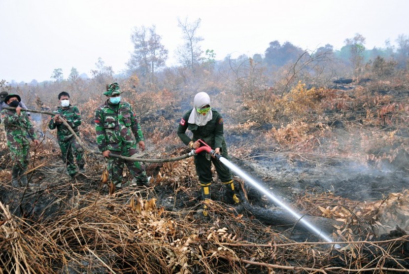 Masitoh (kanan) seorang perempuan anggota pemadam kebakaran Manggala Agni bersama beberapa personel TNI melakukan pemadaman kebakaran di lahan gambut di Rimbo Panjang Kabupaten Kampar, Riau, Rabu (9/9).