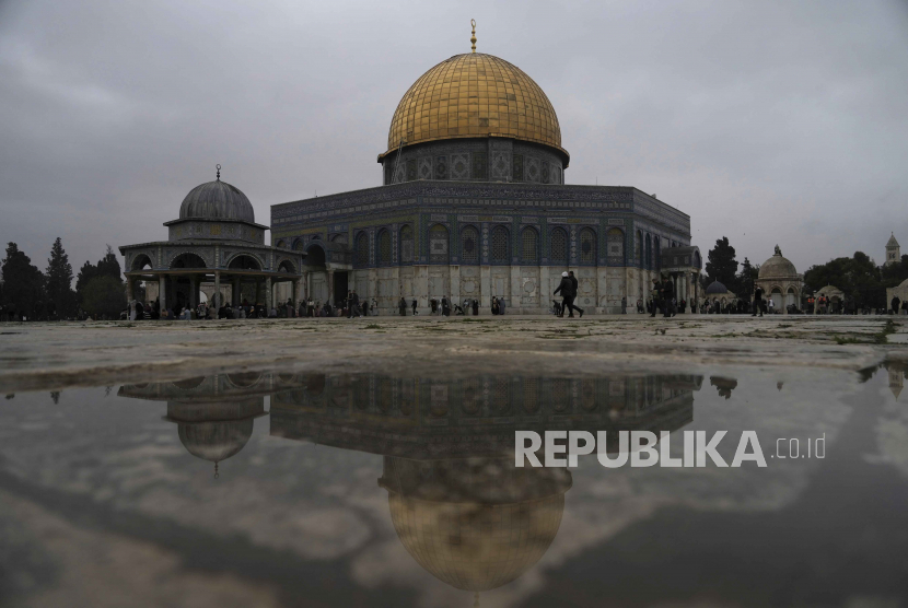Masjid Dome of the Rock tercermin dalam air hujan saat jamaah berkumpul untuk sholat Jumat di hari hujan yang dingin di kompleks Masjid Al-Aqsa di Kota Tua Yerusalem, Jumat (6/1/2023). 