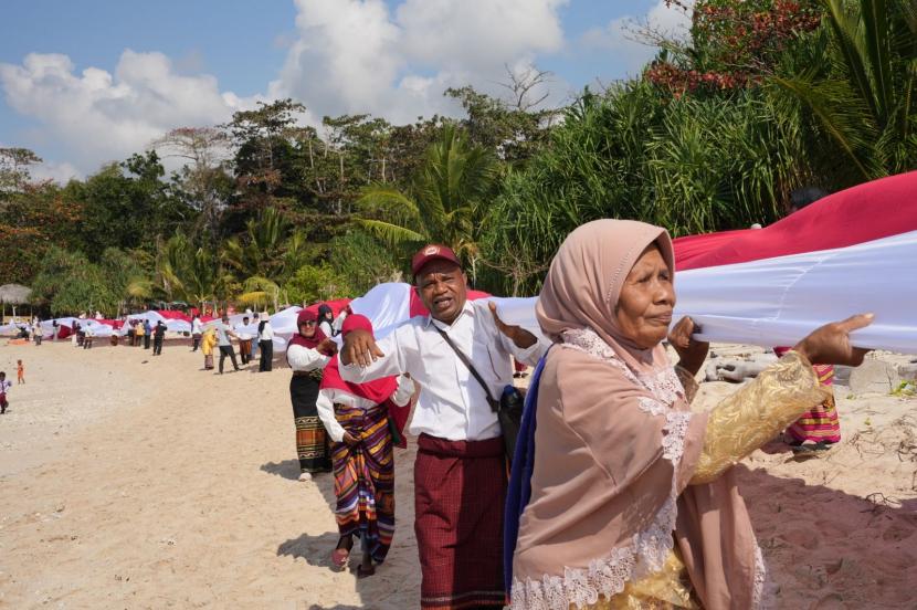 Masyarakat Desa Wowong, Kecamatan Omesuri, Kabupaten Lembata, Nusa Tenggara Timur (NTT) membentangkan bendera merah putih sepanjang satu kilometer di Pantai Nusantara, Sabtu (17/8/2024).  