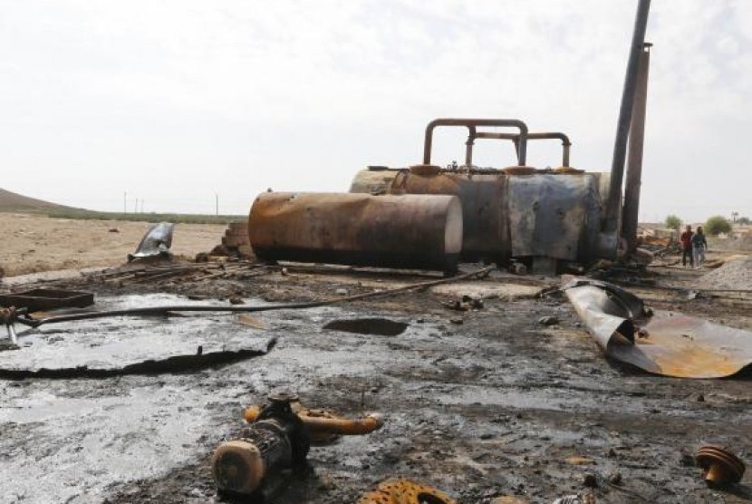 Men walk past damage at an oil refinery and a gas station that were targeted by what activists said were US-led air strikes, in Tel Abyad, near the border with Turkey October 2, 2014. 