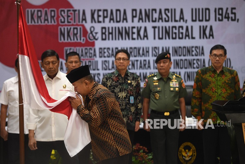 Menko Polhukam Wiranto (kiri) menyaksikan anak pemimpin Darul Islam/Tentara Islam Indonesia (DI/TII) Sekarmaji Marijan Kartosuwiryo, Sarjono Kartosuwiryo (kedua kiri) mencium bendera merah putih dalam acara pengucapan ikrar setia kepada Pancasila, UUD 45, NKRI dan Bhineka Tunggal Ika di Jakarta, Selasa (13/08/2019). 