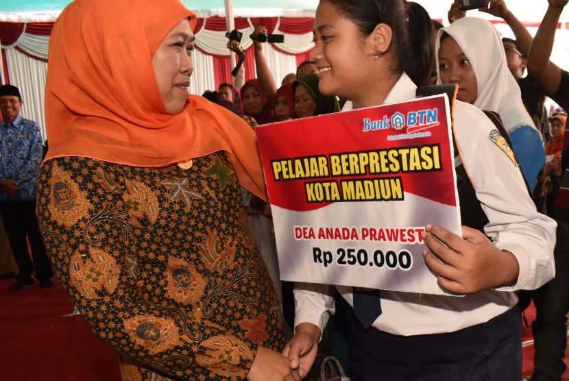 Menteri Sosial Khofifah Indar Parawansa (kiri) menyerahkan beasiswa kepada pelajar berprestasi saat penyaluran bantuan sosial nontunai Program Keluarga Harapan (PKH) di Alun-alun Kota Madiun, Jawa Timur, Senin (17/4). 