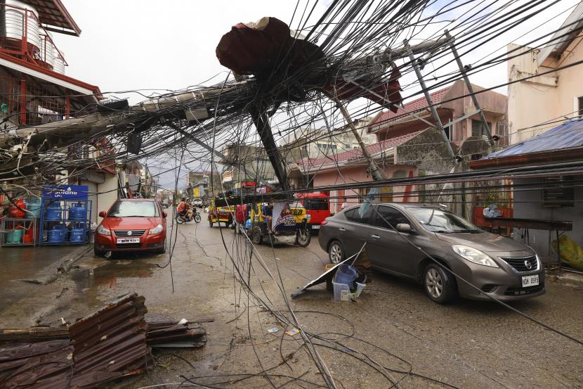 Mobil-mobil melewati tiang listrik yang roboh akibat Topan Rai di kota Surigao, Surigao del Norte, Filipina selatan saat pasokan listrik masih padam pada Minggu 19 Desember 2021. Pemerintah China menyalurkan bantuan untuk ribuan warga Filipina terdampak topan.