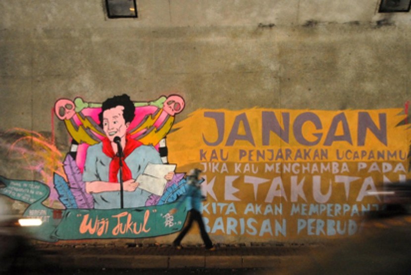 Mural Wiji Thukul Warga melintasi mural bertuliskan 