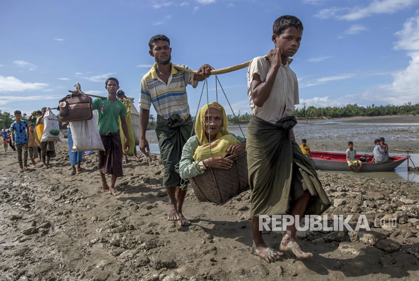 Muslim Rohingya, yang menyeberang dari Myanmar ke Bangladesh, membawa seorang wanita tua masuk dalam keranjang dan berjalan menuju sebuah kamp pengungsi di Shah Porir Dwip, Bangladesh, Kamis, (14/9).