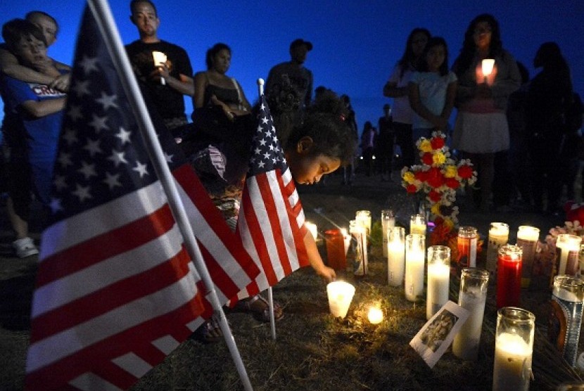 Myia Young (4 years) places a candle by an American flag during a vigil for victims behind a theater where a gunman open fire at moviegoers in Aurora, Colorado July 20, 2012. A total of 71 people were shot in Friday's rampage at the Denver-area movie theat