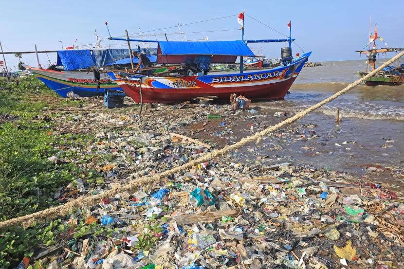 Nelayan memperbaiki perahu di sekitar pantai yang dipenuhi sampah plastik. ilustrasi