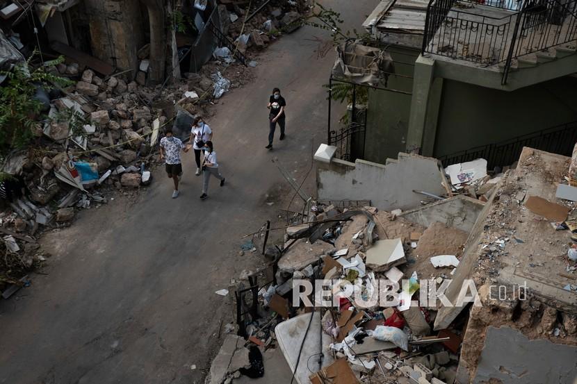 Orang-orang berjalan di dekat puing-puing bangunan yang hancur di lingkungan dekat lokasi ledakan pekan lalu yang melanda pelabuhan Beirut, Lebanon, Kamis (13/8/2020).