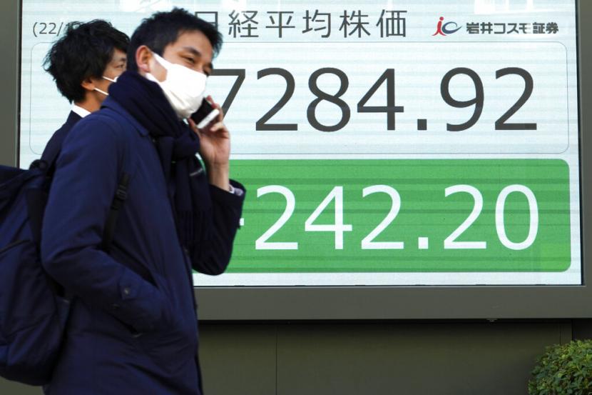 Orang-orang berjalan di depan papan saham elektronik yang menunjukkan indeks Nikkei 225 Jepang di sebuah perusahaan sekuritas pada Senin (19/12/2022).