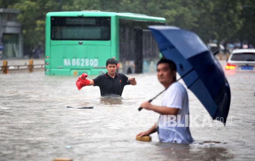  Orang-orang berjalan di jalan yang banjir setelah hujan deras yang melanda kota Zhengzhou di provinsi Henan, China tengah, Selasa, 20 Juli 2021 (dikeluarkan 21 Juli 2021). Banjir besar di China Tengah menewaskan 12 orang di kota Zhengzhou akibat curah hujan kemarin, 20 Juli 2021.