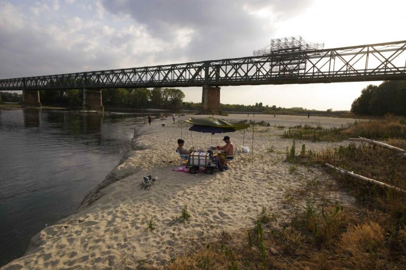 Orang-orang bersantai saat matahari terbenam di dasar sungai Po di sebelah Ponte della Becca (Jembatan Becca) di Linarolo, dekat Pavia, Italia, Senin, 27 Juni 2022.