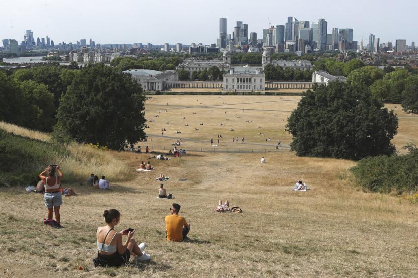 Orang-orang duduk di rerumputan yang dijemur matahari di Greenwich Park dengan latar belakang museum Maritim dan distrik keuangan Canary Wharf di London, Inggris, Ahad, 17 Juli 2022. Presiden Joko Widodo (Jokowi) mengatakan, perubahan iklim menjadi momok yang paling ditakuti dunia saat ini.