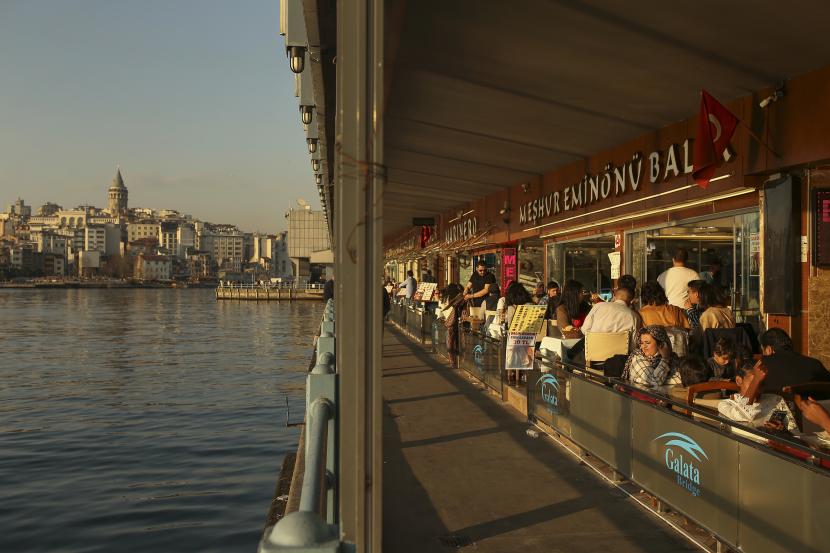 Orang-orang duduk di sebuah restoran di Jembatan Galata di atas Tanduk Emas di Istanbul, Sabtu, 3 April 2021.