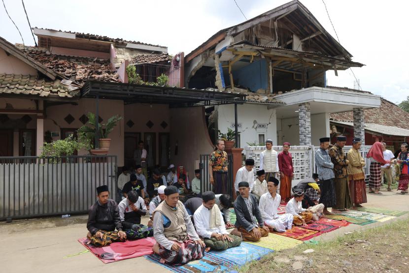 Orang-orang melakukan sholat Jumat di dekat rumah yang rusak akibat gempa Senin, di Cianjur, Jawa Barat, Indonesia, Jumat, 25 November 2022. Gempa berkekuatan 5,6 itu menewaskan ratusan orang, banyak dari mereka anak-anak, dan melukai ribuan lainnya. 