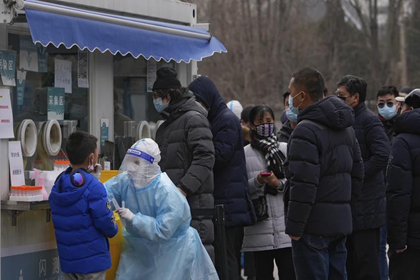 Orang-orang mengantre saat seorang anak laki-laki mengambil sampel usap tenggorokan untuk tes COVID-19 di fasilitas pengujian virus corona seluler di daerah perumahan di Beijing, Rabu, 19 Januari 2022.